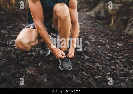 Legatura uomo scarpe da corsa prima di trail running all'esterno. Close-up Foto Stock