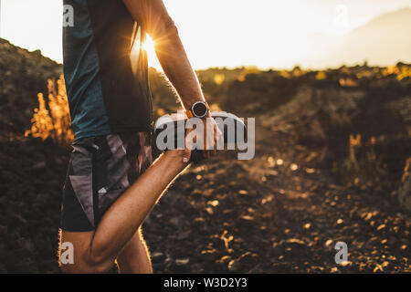 Runner maschio stretching gambe e piedi e preparare per il funzionamento all'aperto. Smartwatches o tracker per il fitness a portata di mano. Bella Luce del sole sullo sfondo. Ac Foto Stock