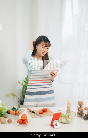 Giovane donna la lettura di un libro di cucina in cucina, cercando ricetta Foto Stock