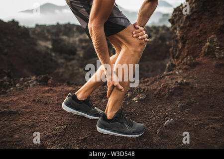 Runner maschio holding feriti muscolo del polpaccio e della sofferenza con dolore. Lo stiramento del legamento mentre è in esecuzione all'esterno. Close-up vista gambe. Foto Stock
