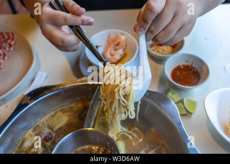 Donna che utilizza bastoncini per prendere tagliatelle in cinese hotpot Foto Stock