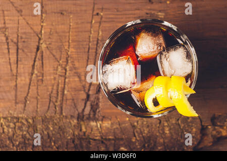 Forte la bevanda alcolica di brandy whiskey in un bicchiere con cubetti di ghiaccio sul legno scuro dello sfondo. Vista superiore . Copia dello spazio. Foto Stock