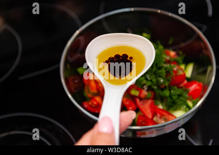 Preparazione di insalata di verdure fresche, cetrioli e pomodori verdi con un bianco cucchiaio di plastica contenente un condimento per insalata realizzato dall'olio d'oliva, Foto Stock