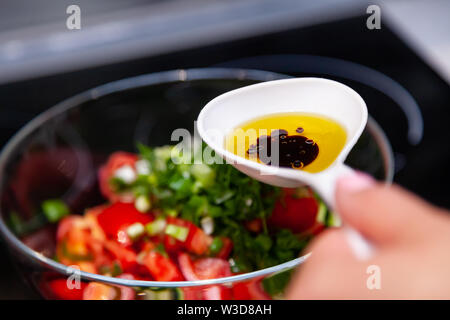 Preparazione di insalata di verdure fresche, cetrioli e pomodori verdi con un bianco cucchiaio di plastica contenente un condimento per insalata realizzato dall'olio d'oliva, Foto Stock