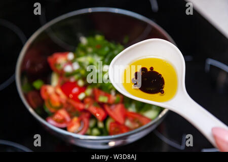 Preparazione di insalata di verdure fresche, cetrioli e pomodori verdi con un bianco cucchiaio di plastica contenente un condimento per insalata realizzato dall'olio d'oliva, Foto Stock