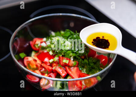 Preparazione di insalata di verdure fresche, cetrioli e pomodori verdi con un bianco cucchiaio di plastica contenente un condimento per insalata realizzato dall'olio d'oliva, Foto Stock