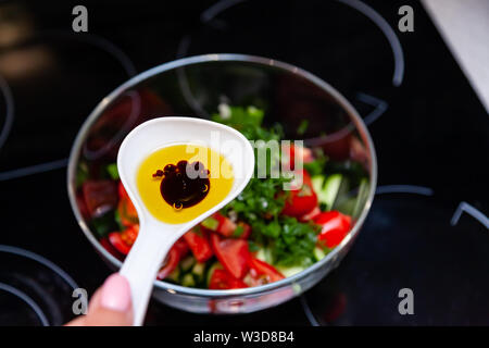 Preparazione di insalata di verdure fresche, cetrioli e pomodori verdi con un bianco cucchiaio di plastica contenente un condimento per insalata realizzato dall'olio d'oliva, Foto Stock
