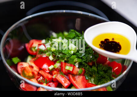 Preparazione di insalata di verdure fresche, cetrioli e pomodori verdi con un bianco cucchiaio di plastica contenente un condimento per insalata realizzato dall'olio d'oliva, Foto Stock