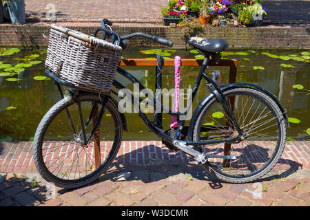 Leiden, Olanda - Luglio 05, 2019: vecchia bicicletta con cestello parcheggiata vicino al piccolo canale Foto Stock