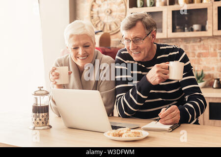 Allegro coppia senior guardando il laptop in cucina Foto Stock