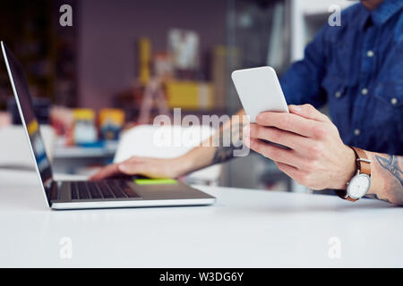 Close-up di giovane uomo usando il telefono e il computer portatile per lo studio mentre è seduto nella biblioteca universitaria Foto Stock