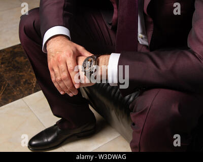 Un uomo in un abito classico è seduta su un divano in pelle nera, close-up, lato destro, vista dall'alto. Dimostrazione di costosi orologi da polso. Lo stile italiano in Foto Stock