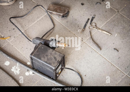 Industrial pistola per saldatura di colore nero sul pavimento tra polvere e strumenti per il riscaldamento e fusione di plastica durante il collegamento di parti in worksh Foto Stock