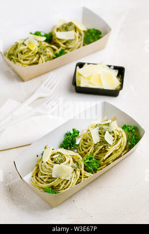 Pasta al pesto decorate con parmigiano e prezzemolo riccio in un tradizionale take-away box dal ristorante su sfondo bianco Foto Stock