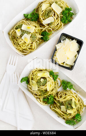 Pasta al pesto decorate con parmigiano e prezzemolo riccio in un tradizionale take-away box dal ristorante su sfondo bianco Foto Stock