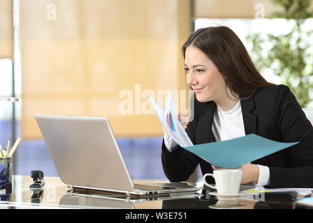 Serie Executive confrontando laptop contenuti online e dei documenti cartacei in ufficio Foto Stock