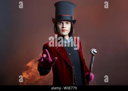 Favoloso circus uomo in un cappello e un abito rosso in posa il fumo su un colore di sfondo scuro. Un clown in un party, uomo gentleman da una fiaba. Wiz Foto Stock