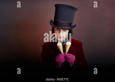 Favoloso circus uomo in un cappello e un abito rosso in posa il fumo su un colore di sfondo scuro. Un clown in un party, uomo gentleman da una fiaba. Wiz Foto Stock