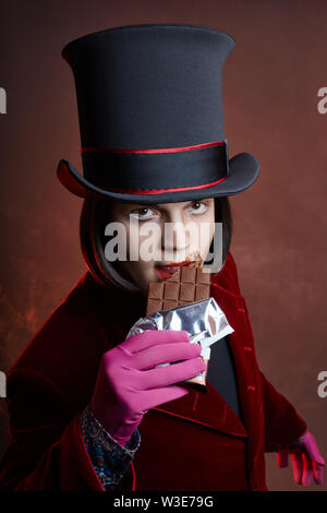 Favoloso circus uomo in un cappello e un abito rosso in posa il fumo su un colore di sfondo scuro. Un clown in un party, uomo gentleman da una fiaba. Wiz Foto Stock