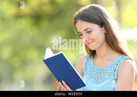 Grave donna la lettura di una carta vergine libro su sfondo verde in un parco Foto Stock