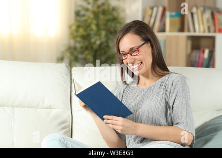 Felice donna che indossa gli occhiali per leggere un libro seduti su un divano nel salotto di casa Foto Stock