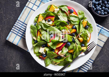 Close-up di insalata con fresche foglie di bietole, pesche, mirtilli, pezzi di formaggio gorgonzola servita su una piastra bianca su una tabella di calcestruzzo con ingrediente Foto Stock