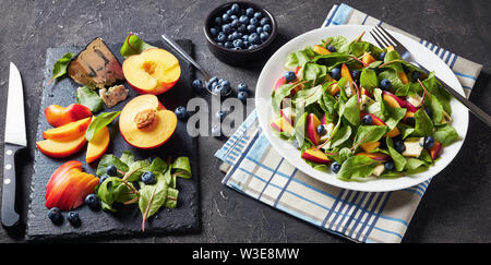 Insalata con fresche foglie di bietole, pesche, mirtilli, pezzi di formaggio gorgonzola servita su una piastra bianca su una tabella di calcestruzzo con ingredienti, horizonta Foto Stock