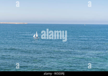 Un solitario barca a vela vele sull'azzurro del mare calmo su una soleggiata giornata estiva. Il concetto di viaggio e di pacificazione Foto Stock