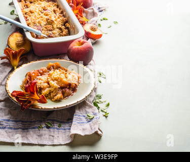 Peschi gustosi dessert sbriciolare in piastra su sfondo chiaro con teglia da forno e pesche fresche . Spazio di copia Foto Stock