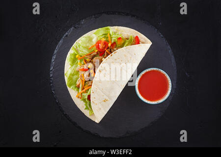 Burrito si avvolge con il pollo e le verdure su nero ardesia. Burrito di pollo, cibo messicano Foto Stock