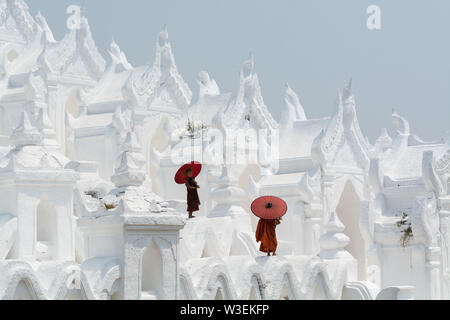 Mandalay, Myanmar - Aprile 2019: buddista novizio monaci in arancione vesti con red ombrelloni a camminare sulle pareti della Pagoda Myatheindan. Foto Stock