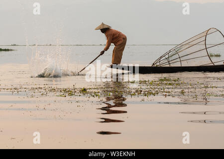 Inle, Myanmar - Marzo 2019: tradizionale birmana gamba pescatore di canottaggio a Lago Inle durante il sunrise smashing acqua con paddle Foto Stock