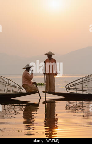 Inle, Myanmar - Marzo 2019: tradizionale birmana gamba pescatori di canottaggio a Lago Inle durante il sunrise. Seduto sulla barca e fumatori. Foto Stock