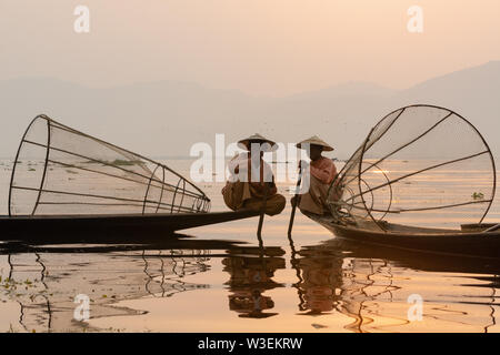 Inle, Myanmar - Marzo 2019: tradizionale birmana gamba pescatori di canottaggio a Lago Inle durante il sunrise. Seduto sulla barca e fumatori. Foto Stock