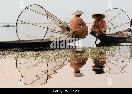 Inle, Myanmar - Marzo 2019: tradizionale birmana gamba pescatori di canottaggio a Lago Inle durante il sunrise. Seduto sulla barca e fumatori. Foto Stock