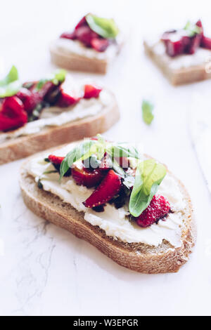 Sandwich con fragole, formaggio morbido e aceto balsamico su una luce Sfondo marmo. Foto Stock