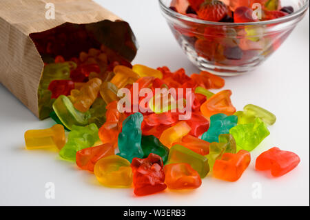 Ciotole in vetro e sacchetto di carta colorata di caramelle gommose su sfondo bianco Foto Stock