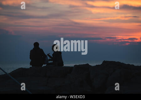 Giovane seduto sulla scogliera di roccia guardando il tramonto. romantico data. vacanze estive Foto Stock