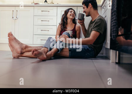 Felice coppia giovane rilassante in cucina con accessori per caffè. Giovane uomo e donna seduta sul pavimento della cucina di bere il caffè Foto Stock