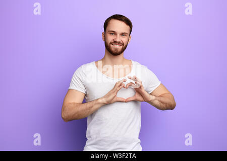 Allegro bello ragazzo che mostra il simbolo del cuore e la forma con le mani. Concetto romantico.sentimento e emozione isolati a sfondo blu. Foto Stock