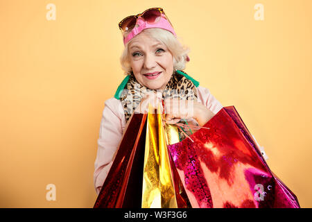 Sorridente elegante old Lady facendo shopping. granny godendo di giornata di acquisti isolati a sfondo giallo . tempo libero, tempo di ricambio Foto Stock