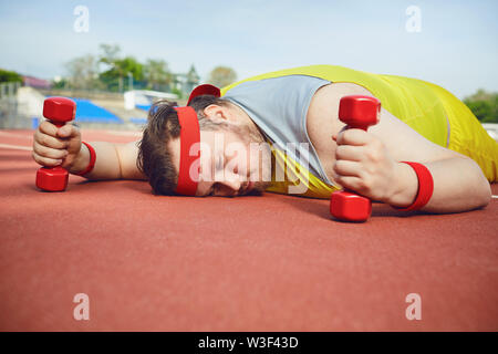 Fat lazy uomo dorme stanco giace sulla pista dello stadio. Il concetto di perdere il peso, la dieta. Foto Stock