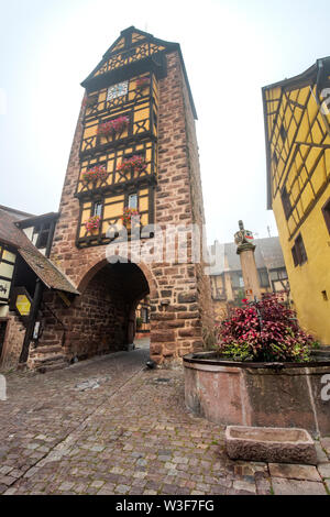 Old town gate del villaggio con Riquewihr timberwork, Alsazia strada del vino, Francia, il Landmark Tower Dolder e fiore-adornato ben Foto Stock