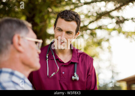 Sorridente infermiera maschio assistere un paziente anziano all'esterno. Foto Stock