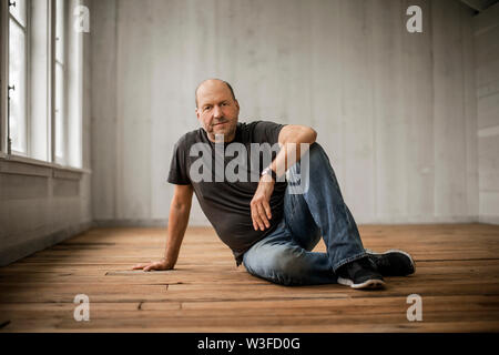 Ritratto di un uomo di mezza età seduto su un pavimento di legno. Foto Stock