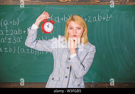 Ella si occupa circa la disciplina. Insegnante di donna tenere premuto il tasto alarm clock. Girl School docente. A che ora è. Orario delle lezioni. Benvenuti insegnante anno scolastico. Salute e regime quotidiano. Educatore avvia lezione. Foto Stock