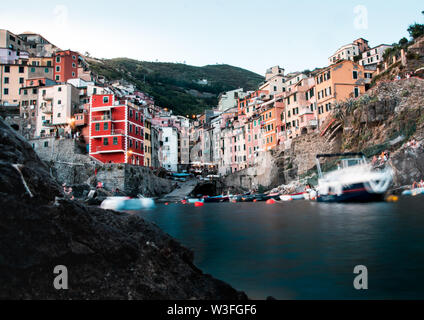 Una delle Cinque Terre Riomaggiore città fotografata da un angolo basso sull'acqua come una lunga esposizione Foto Stock