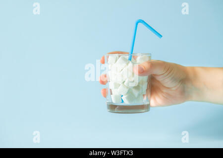 Eccessivo consumo di zucchero concetto - la mano che regge il vetro con cubetti di zucchero Foto Stock