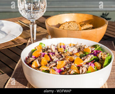 Estate cibo: insalata di sgombro pasto con le clementine e barbabietole servita all'aperto in bianco stoviglie con baguette di pane nella ciotola di legno e vetro del vino Foto Stock