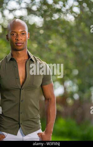 Ritratto di un uomo in posa parzialmente staccata dal telaio. Giovane americano africano modello maschile in una scena naturale sfondo sfocato Foto Stock